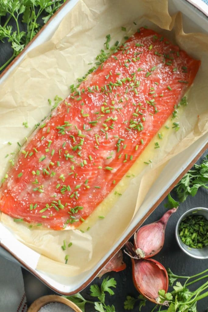 Slow roasted salmon with butter, salt, and chives over it in a baking dish.